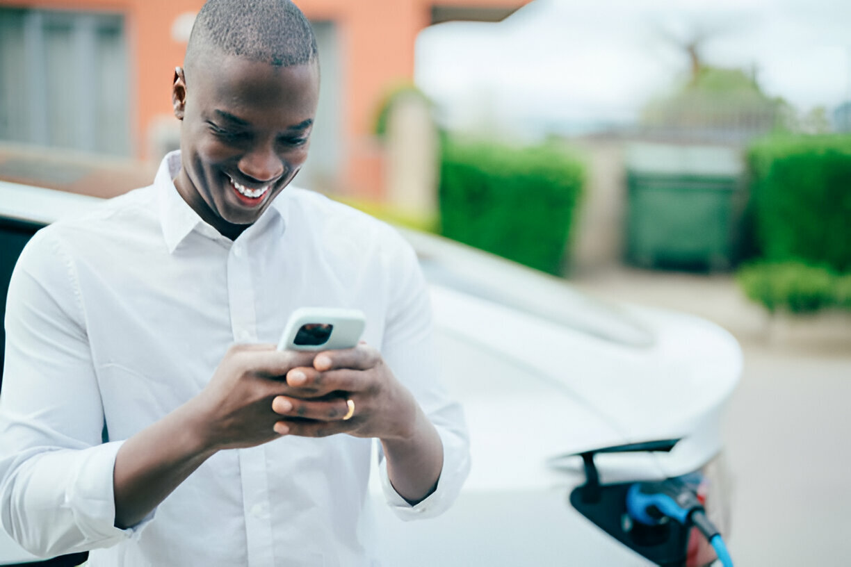 Nigerian Man texting on phone while charging electric car